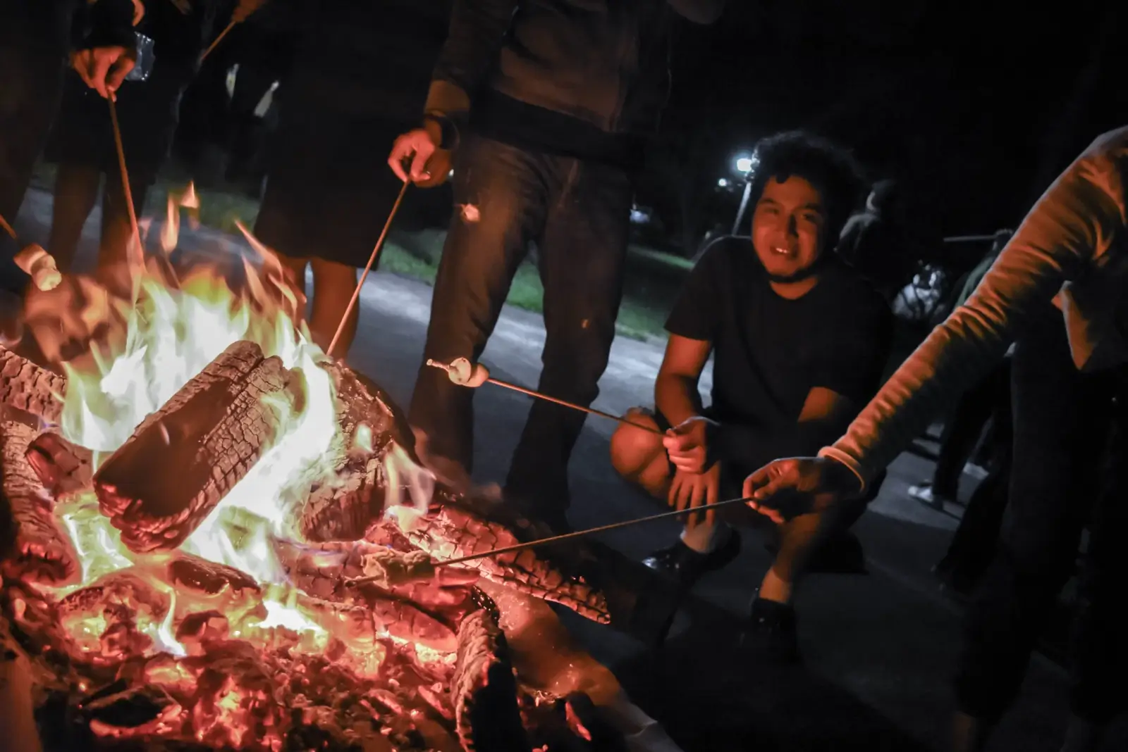 A man smiling with a group of friends roasting marshmallows over a campfire in St. Lucie.