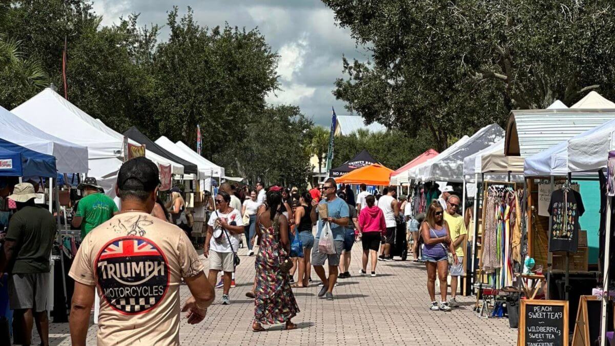 A crowd of people shop vendor tents at a farmers market in St. Lucie, Florida. 